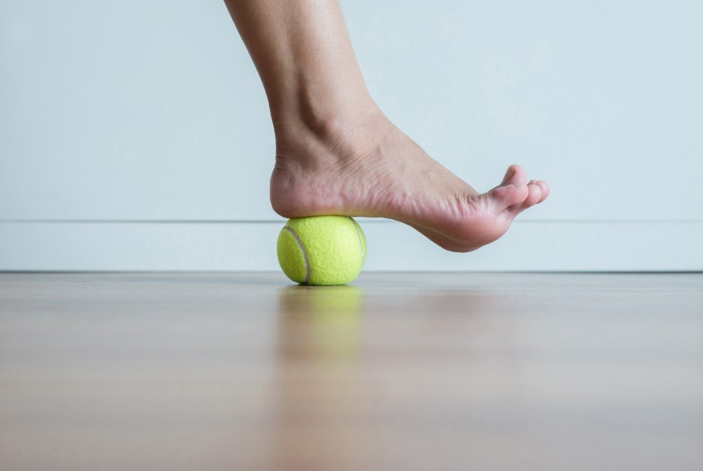 Woman massages her foot with a tennis ball. Feet soles or heel massage for plantar fasciitis.